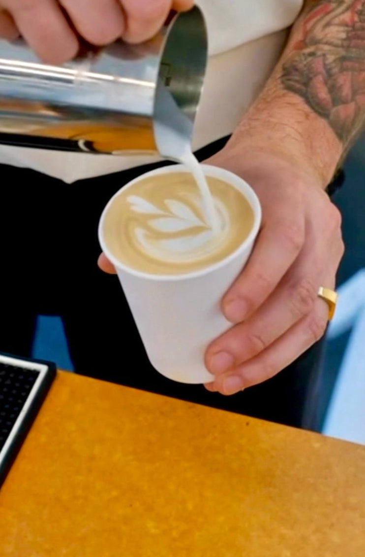 Person pouring milk into a coffee cup with latte art