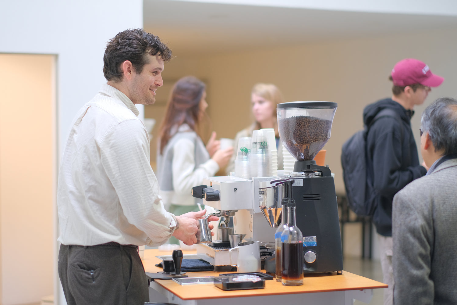 Person using a coffee machine at an event with other attendees in the background